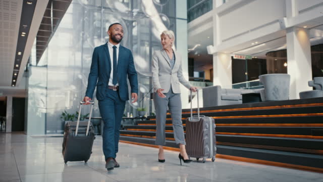 Travel, business and people with luggage talking and walking through hotel, airport or conference hall, happy and positive. Man and woman corporate partners on trip with suitcase through hallway