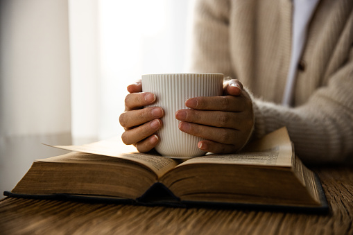 Woman hand holding coffee cup and reading a book