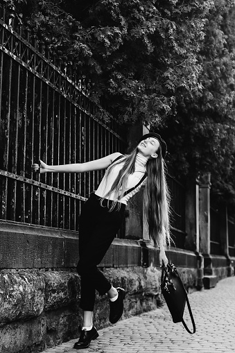 a dreamed girl holds her hand behind the fence by lifting one leg on a black and white photo