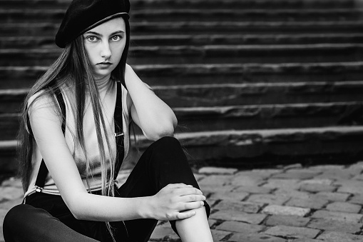 close-up fragile girl which sits on the sidewalk on the background of stairs in black white photography