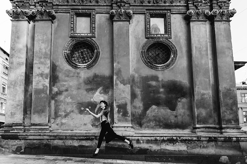 girl during an elegant jump on the street against the background of a building with old architecture on a black and white photo