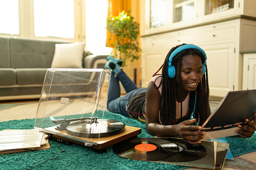 A young woman lying on the floor near a turntable and listening to the vinyl record music on her headphones