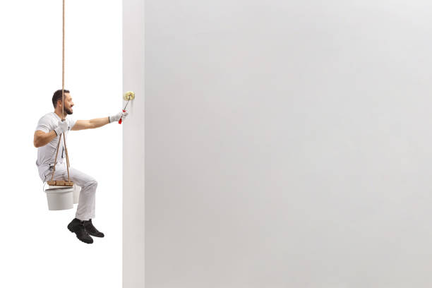 istock Painter sitting on a swing and painting a wall with a roller 1436358064