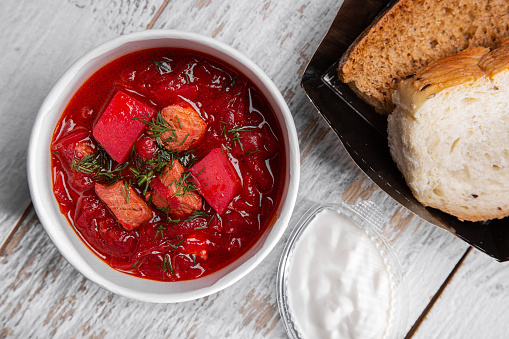 Borsch with meat, beets, potatoes and parsley in a plate on the table with bread and sour cream