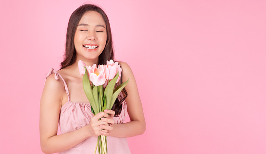 Beautiful asian woman holding bouquet tulips smell standing on pink background. Close up happy portrait young girl smiling freshness hold blossom pink tulips with copy space over isolated. Celebrate