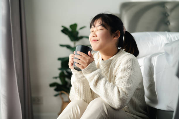 istock Young woman drinking coffee in bedroom, Holding coffee cup with two hands 1436360814