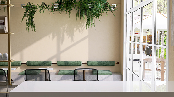 White counter of modern and cozy cafe and restaurant with coffee table and  green cushion chair decorated with plants on beige wall with sunlight from glass door to outdoor garden
