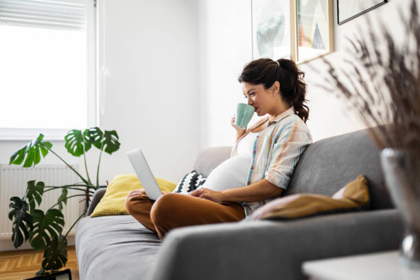 istock Happy pregnant woman using laptop drinking coffee 1436361900