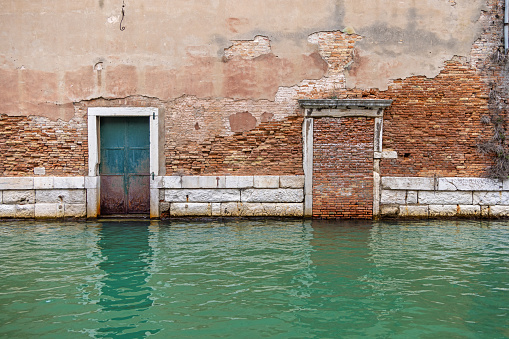 Walled up doorway in a brownstone wall facing a canal in the center of the old and famous Italian city Venice