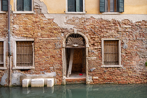 Doorway in a old and weathered brownstone wall facing a canal in the center of the old and famous Italian city Venice