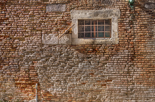 Window in a old weathered brownstone wall in the center of the old Italian city Venice
