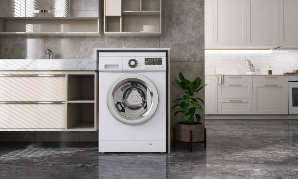 Modern and luxury design of beige laundry room with washing machine, counter, cabinet, shelf connected to kitchen on black granite tile floor with sunlight from window blinds stock photo