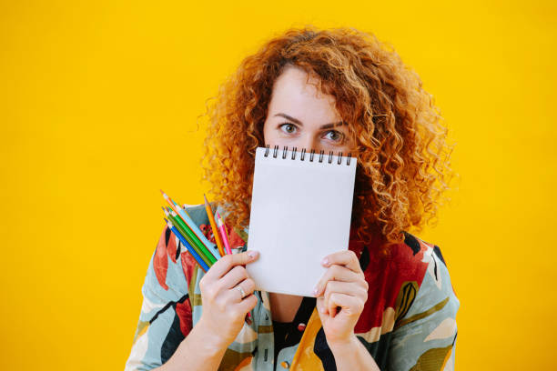 istock Staring young woman looking over her notebook, covering her face. 1436371346