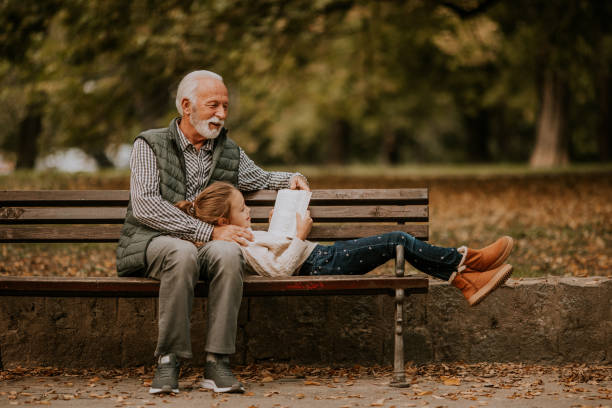 Grandfather spending time with his granddaughter on bench in park on autumn day Handsome grandfather spending time with his granddaughter on bench in park on autumn day sitting on bench stock pictures, royalty-free photos & images