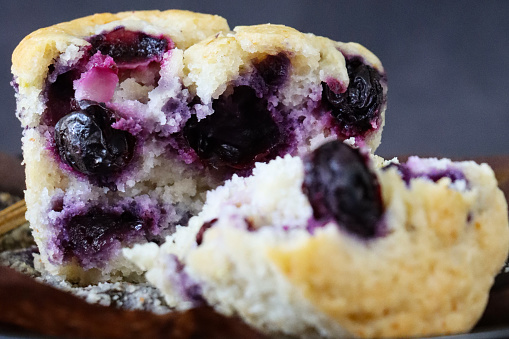 Stock photo showing close-up, elevated view of black cake stand containing an individual blueberry muffin unwrapped from a brown paper cake case, against a mottled grey background. Home baking concept.