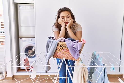 Young hispanic girl tired leaning on laundy basket at home
