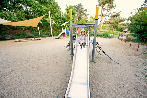 Baby girl slides in children's playground toy set in public park.