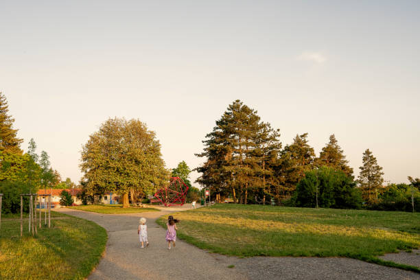 Back of two sisters run to playground in park.