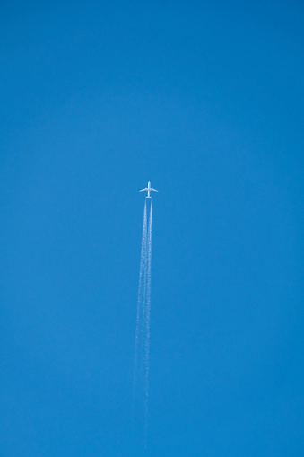 Distant passenger jet plane flying on high altitude on clear blue sky leaving white smoke trace of contrail behind. Air transportation concept.