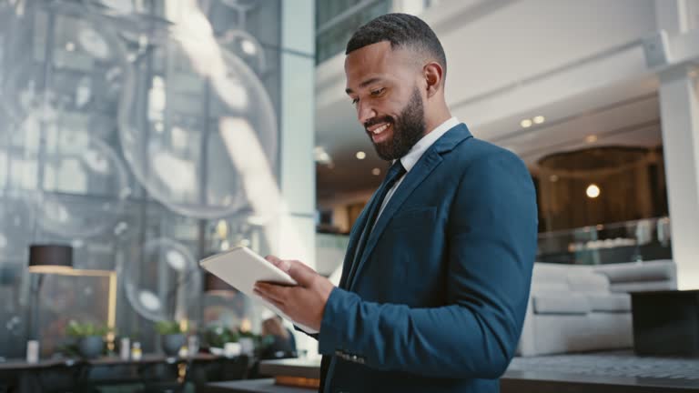 Corporate, black man and tablet working of a businessman happy with technology in a hotel. Digital, internet and web company growth planning of a entrepreneur online with a smile typing a job email