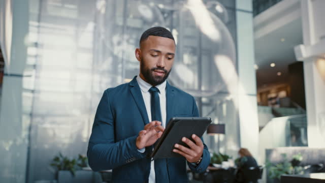 Businessman working on a digital tablet while walking in a corporate office. Marketing professional and black man doing research on the internet or a website with a mobile device fordstart project