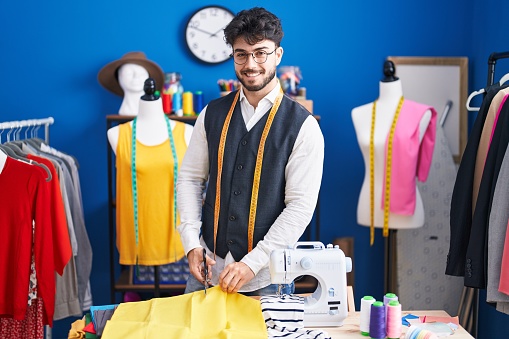Young hispanic man tailor smiling confident cutting cloth at sewing studio
