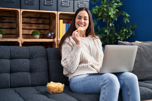 Young woman using smartphone and eating chips potatoes at home
