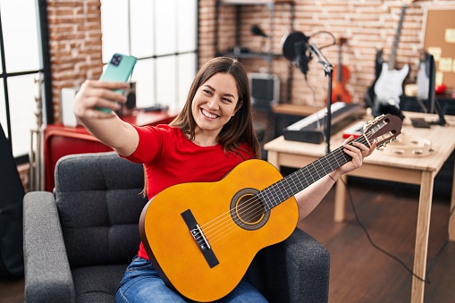 Young woman musician make selfie by smartphone playing classical guitar at music studio
