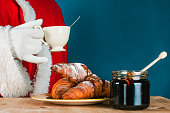 Santa Claus in celebration. Tea or coffee drinking with croissants and honey. Happy and delicious Christmas holiday.