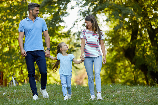 Happy young family of three holding hands and smiling while walking in park