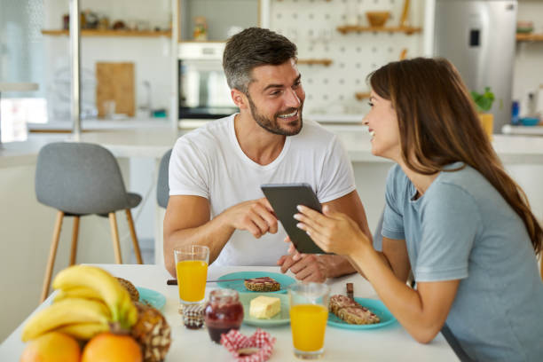Happy young couple using a digital tablet during breakfast at home stock photo
