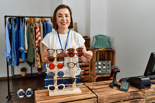 Middle age hispanic woman working selling sunglasses at retail shop