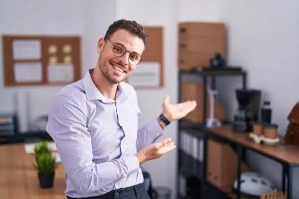 Young hispanic man at the office inviting to enter smiling natural with open hand