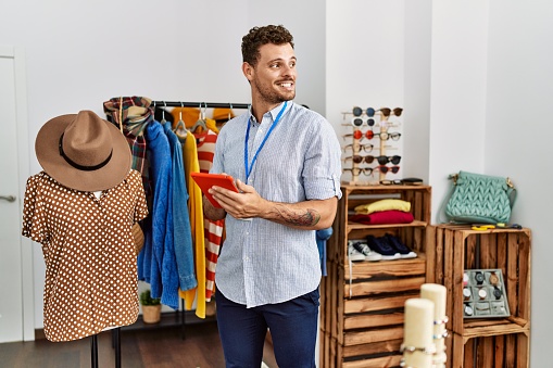 Young hispanic shopkeeper man smiling happy using touchpad working at clothing store.