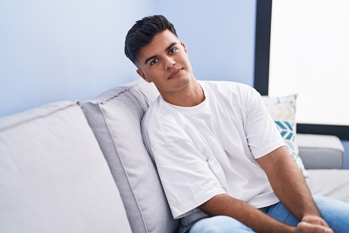 Young hispanic man sitting on sofa with relaxed expression at home