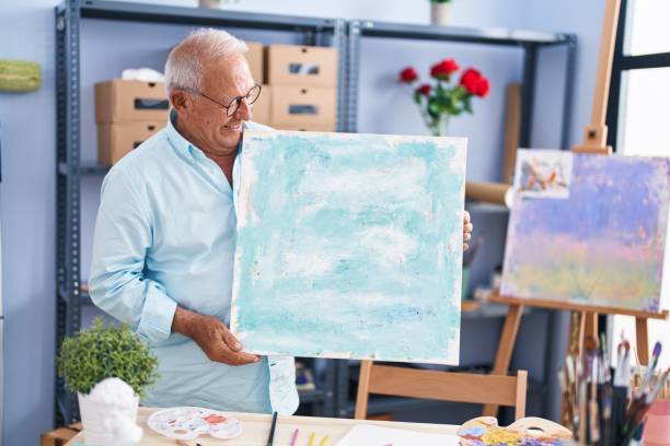 istock Senior grey-haired man artist smiling confident holding draw at art studio 1436384023