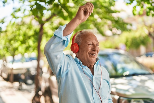 Senior grey-haired man listening to music and dancing at street
