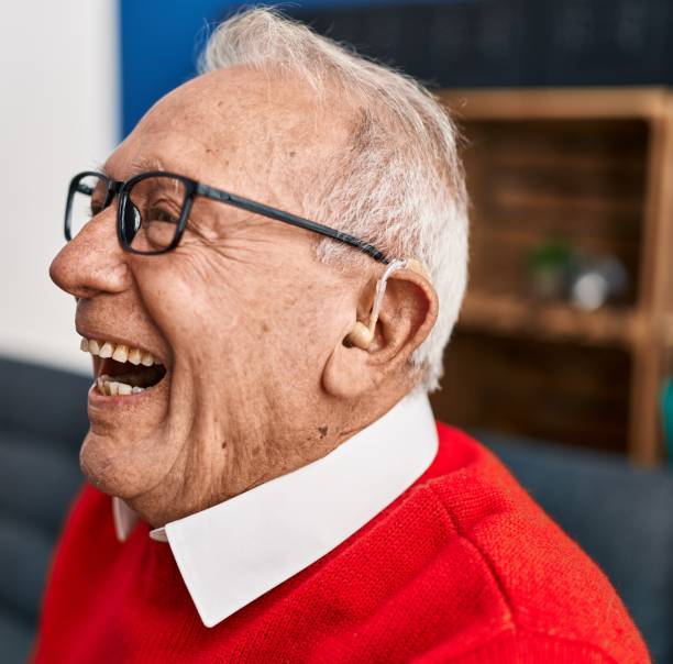 Senior man smiling confident using deafness hearing aid at home stock photo