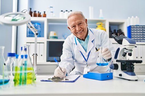 Senior man wearing scientist uniform measuring liquid at laboratory