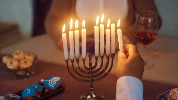 Close up of Jewish man lighting candles in menorah at home. Close up of senior man lighting the menorah during Hanukkah celebration. orthodox judaism photos stock pictures, royalty-free photos & images