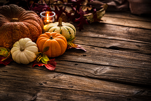 Autumn or Thanksgiving decoration: gourds, dry leaves and burning candle shot on rustic wooden table. The composition is at the top left of an horizontal frame leaving useful copy space for text and/or logo. High resolution 42Mp studio digital capture taken with SONY A7rII and Zeiss Batis 40mm F2.0 CF lens