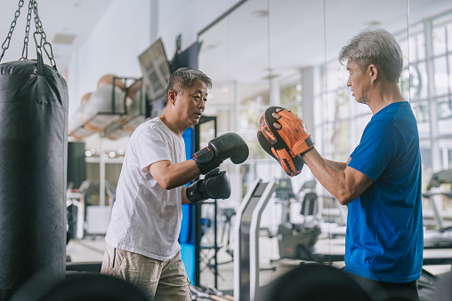 Asian Chinese Senior Men practicing boxing sparring in gym on routine weekend activity