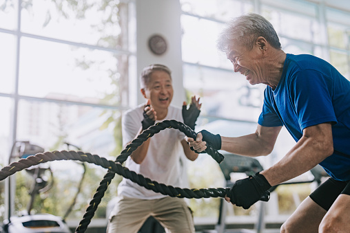 Asian Chinese Senior personal trainer encouraging senior man practicing battle rope in gym