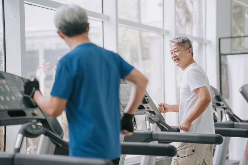 2 senior Chinese men running on treadmill in gym together