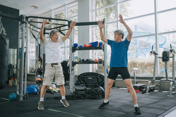 2 chinese senior men jumping jack side by side in gym 2 chinese senior men jumping jack side by side in gym JUMPING JACKS stock pictures, royalty-free photos & images