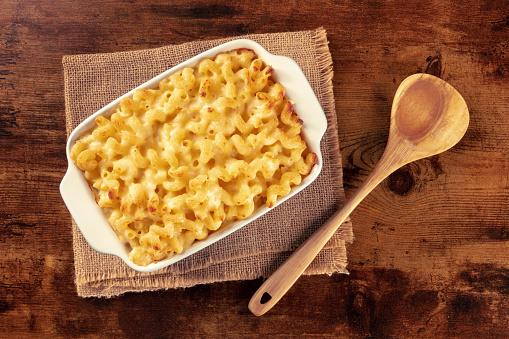 Macaroni and cheese pasta in a casserole, shot from above on a rustic table with a wooden spoon