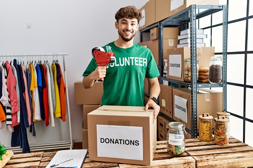 Young . man wearing volunteer uniform packing donations box at charity center