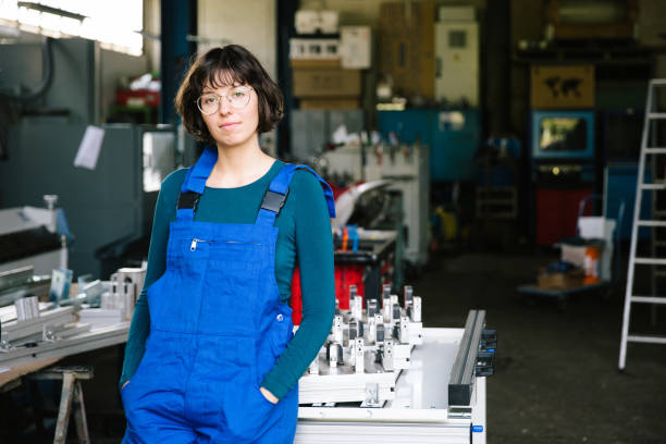 Portrait of a smiling young female trainee in metal industry, hands in pockets stock photo
