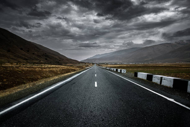 Infinite asphalt road with marking at stormy weather and rain clouds