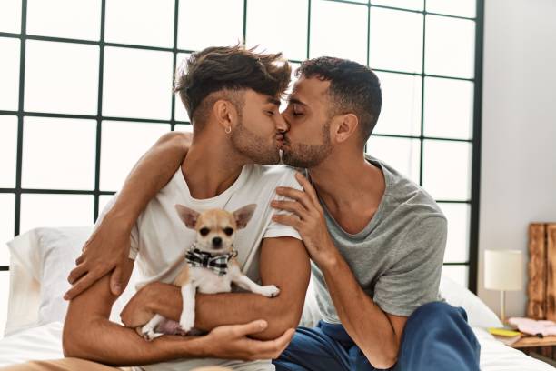 寝室でチワワと一緒にベッドに座ってキスをして抱きしめる2人の��ヒスパニック系男性 - gay man homosexual men kissing ストックフォトと画像